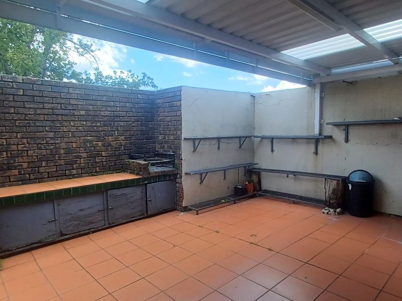 Covered outdoor patio featuring a built-in braai, tiled flooring, utility sink, and wall-mounted shelving, offering a functional space for outdoor entertaining.