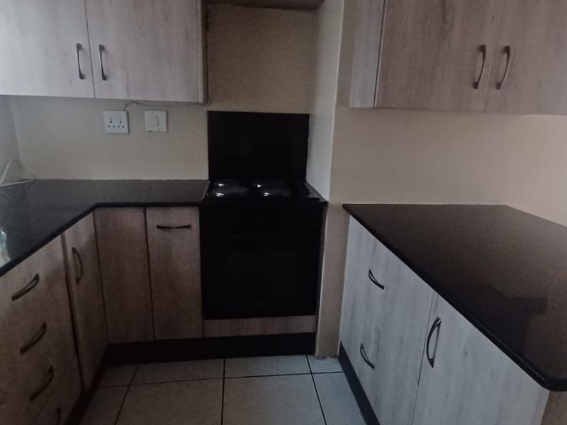 A functional kitchen featuring modern wood-look cabinetry, dark granite countertops, and a built-in electric stove and oven with tiled flooring.