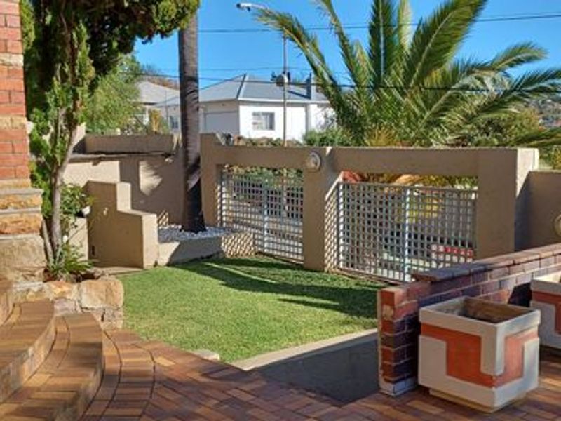 A paved outdoor patio area featuring brick stairs, built-in planters, and a secure metal gate leading to the street.