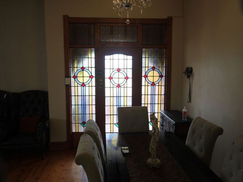 An elegant entrance area featuring a classic timber door with intricate stained glass panels, complemented by polished hardwood flooring and a decorative chandelier.