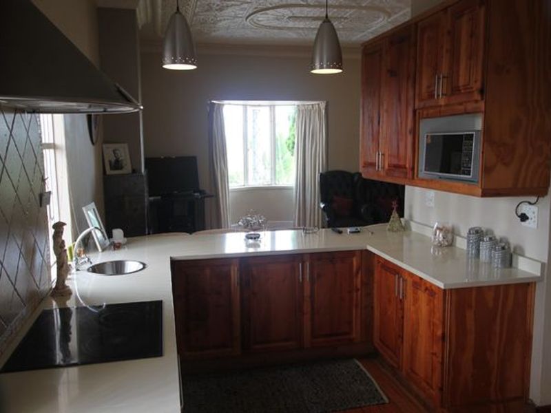 A functional kitchen featuring warm wooden cabinetry, stone countertops, integrated appliances, and a decorative pressed metal ceiling.