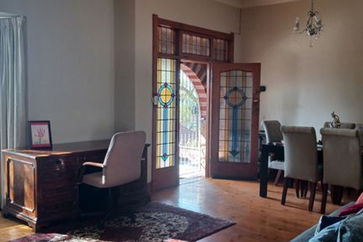 Spacious living area featuring original hardwood flooring, a classic bay window, and elegant stained glass double doors leading to the exterior.