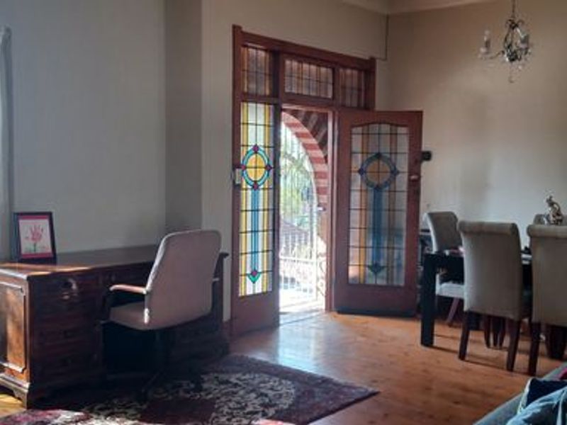 Spacious living area featuring original hardwood flooring, a classic bay window, and elegant stained glass double doors leading to the exterior.