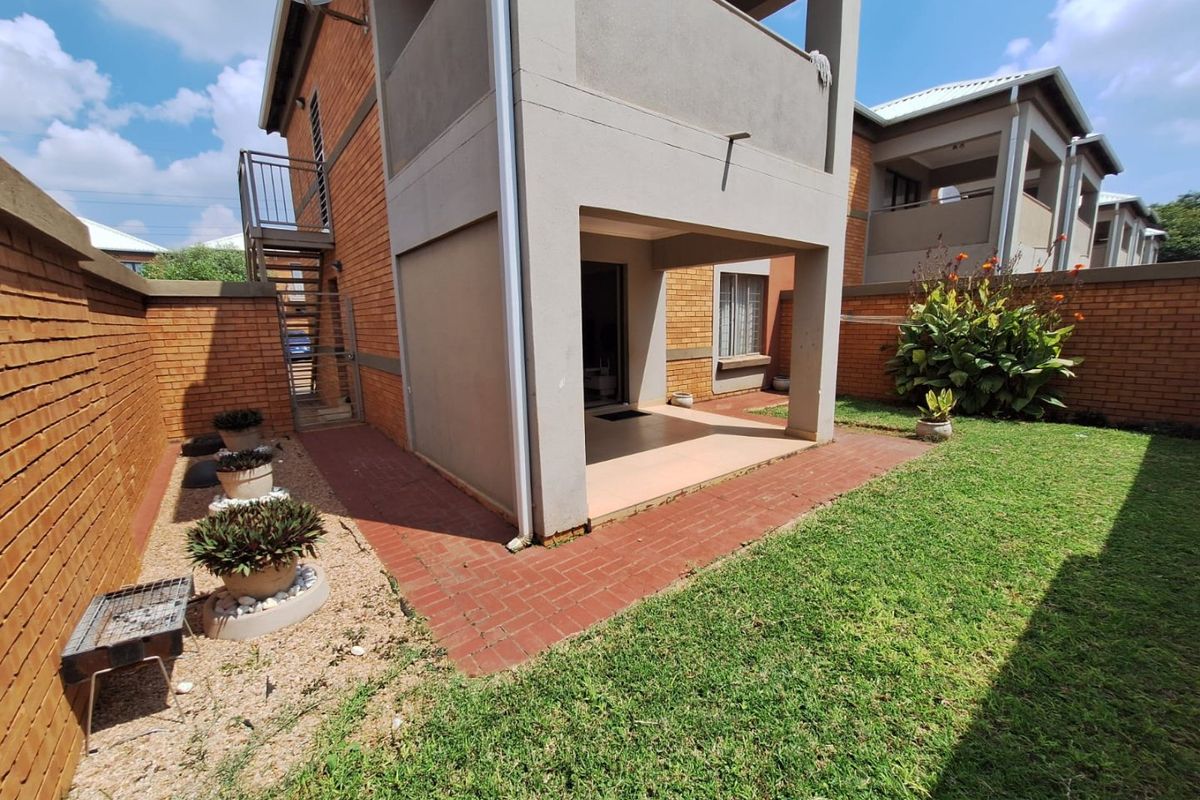 A private rear garden featuring a paved patio area, established lawn, and brick boundary walls, providing a functional outdoor space for the apartment.