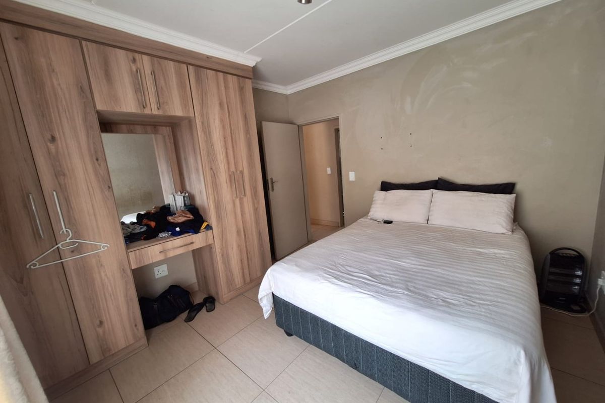 A bedroom featuring built-in wooden cupboards with an integrated vanity mirror and tiled flooring.