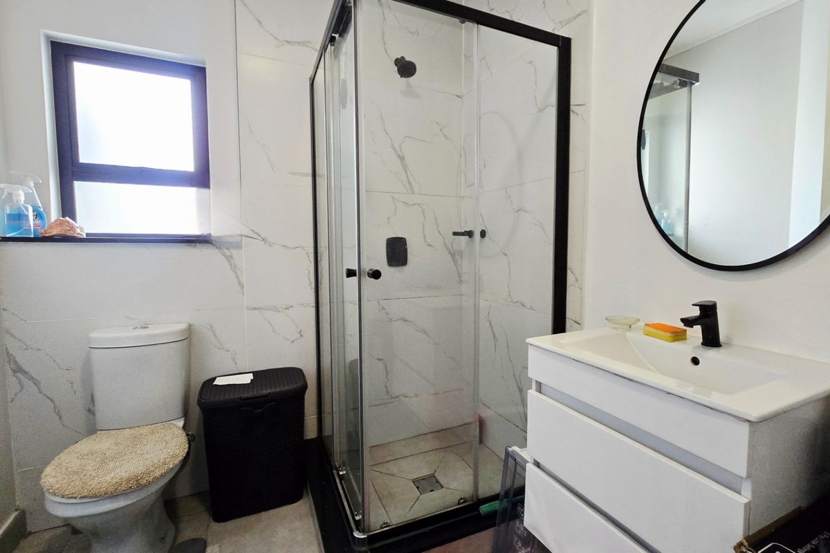 Modern bathroom featuring a glass shower enclosure, vanity cabinet with basin, and marble-look wall tiling.