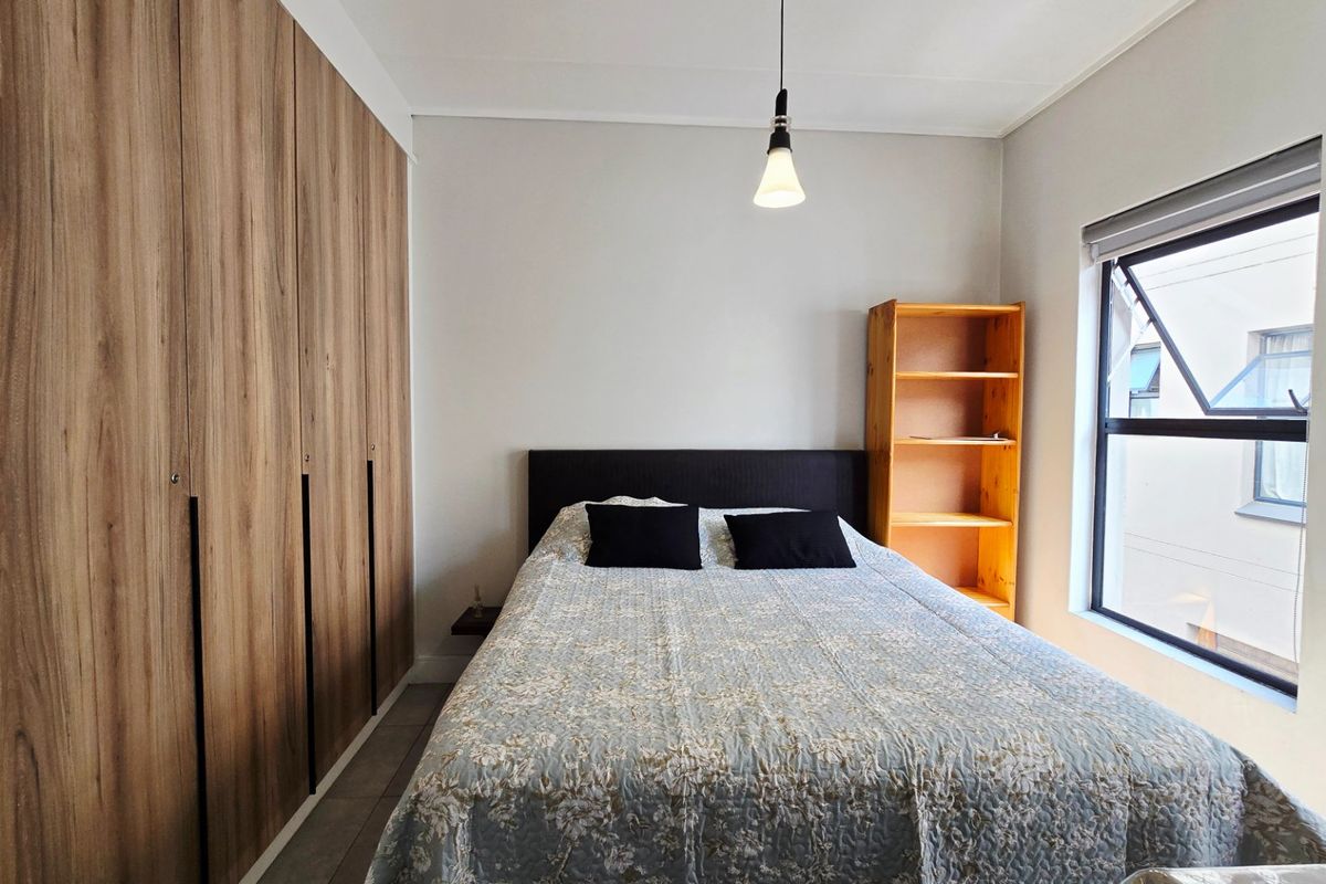 A well-maintained bedroom featuring floor-to-ceiling built-in cupboards, neutral wall finishes, and a top-hung window with a roller blind.