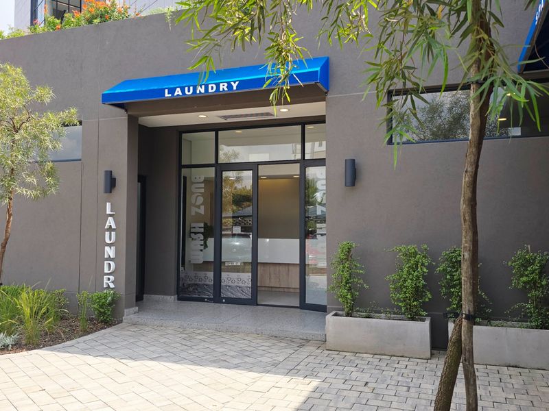 Exterior view of the apartment complex laundry and spa facility entrance, featuring modern signage, glass doors, and landscaped concrete planters.