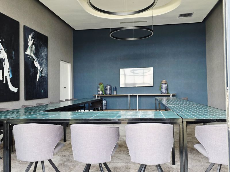 A modern, well-appointed clubhouse meeting space featuring a large tiled table, recessed ceiling detail, and contemporary pendant lighting.