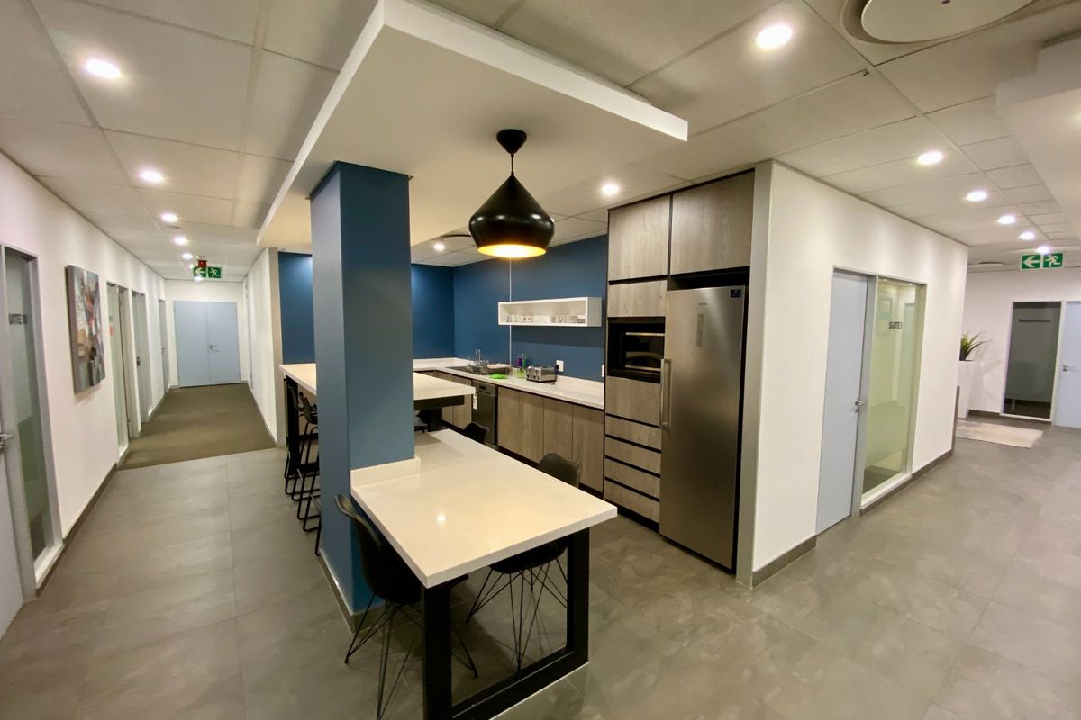 Modern commercial kitchenette featuring sleek cabinetry, stone countertops, integrated oven, and contemporary pendant lighting, set within a professional office environment.