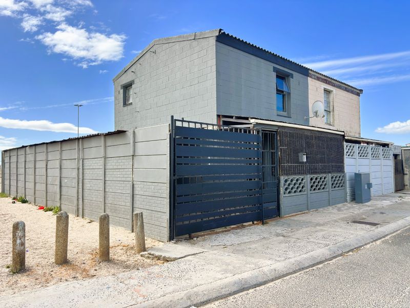 Front exterior view of a two-story house featuring a concrete block boundary wall, metal security gate, and paved street frontage.