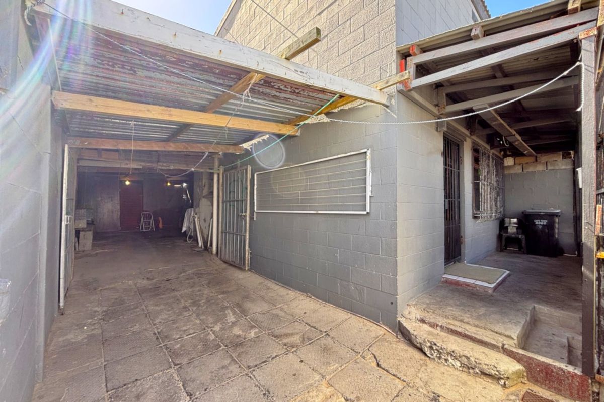 Rear exterior area featuring a paved courtyard, concrete block walls, and a covered structure with corrugated metal roofing.