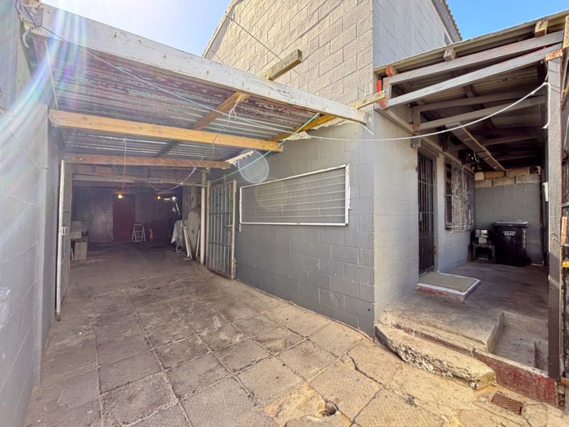Rear exterior area featuring a paved courtyard, concrete block walls, and a covered structure with corrugated metal roofing.