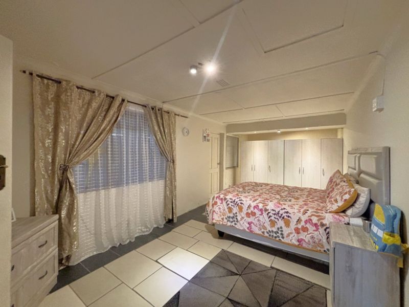 Spacious bedroom featuring built-in cupboards, tiled flooring, and a neutral ceiling finish, offering a functional layout with ample storage space.