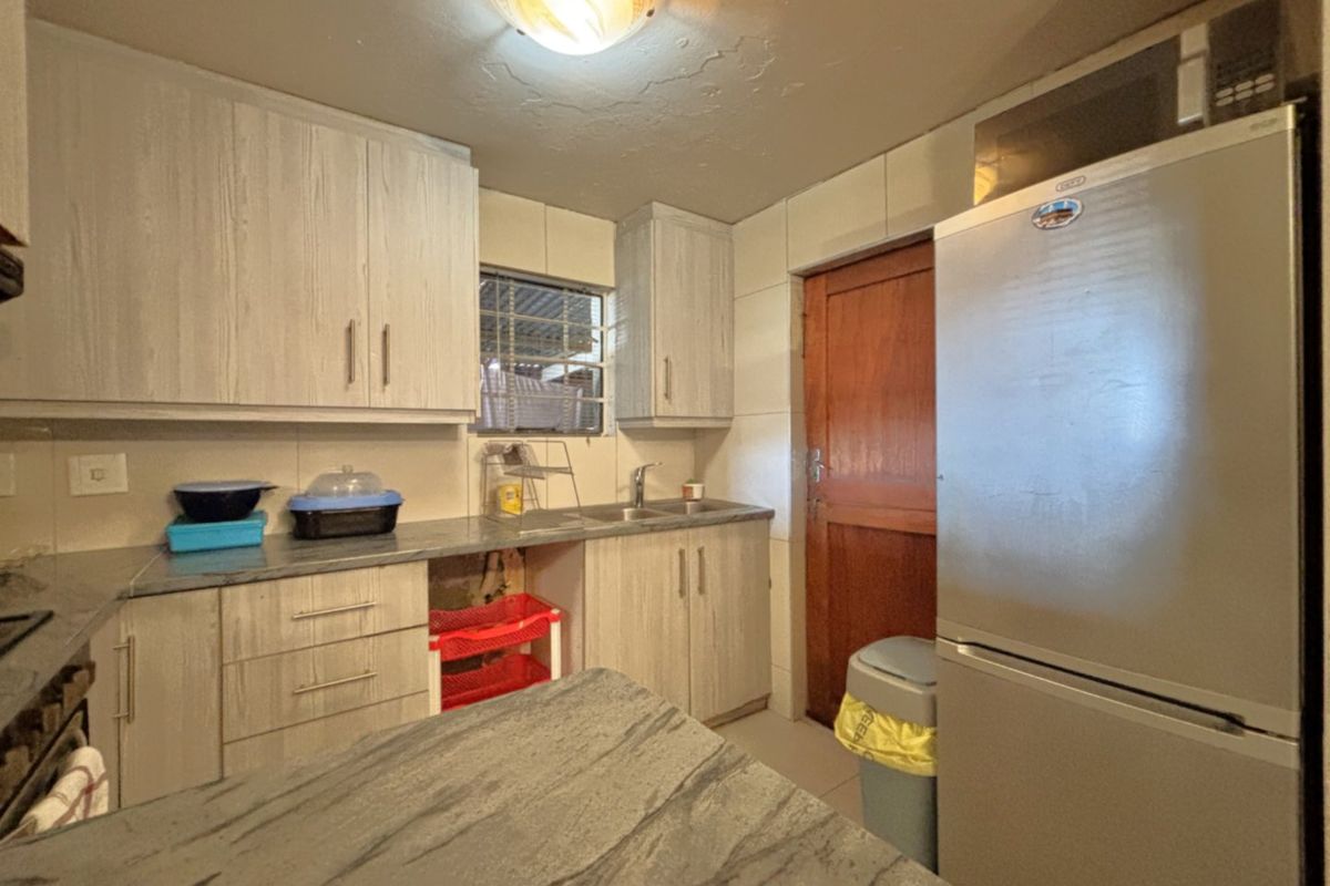 Compact kitchen featuring light wood-grain cabinetry, laminate countertops, tiled backsplash, and integrated microwave, offering a functional layout with potential for modern updates.