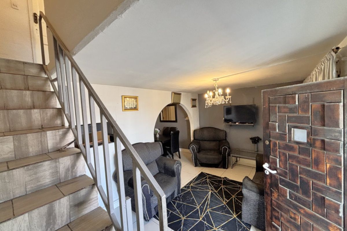 Living room area featuring a tiled staircase with metal balustrade, arched architectural detail, and tiled flooring, providing a functional open-plan layout.