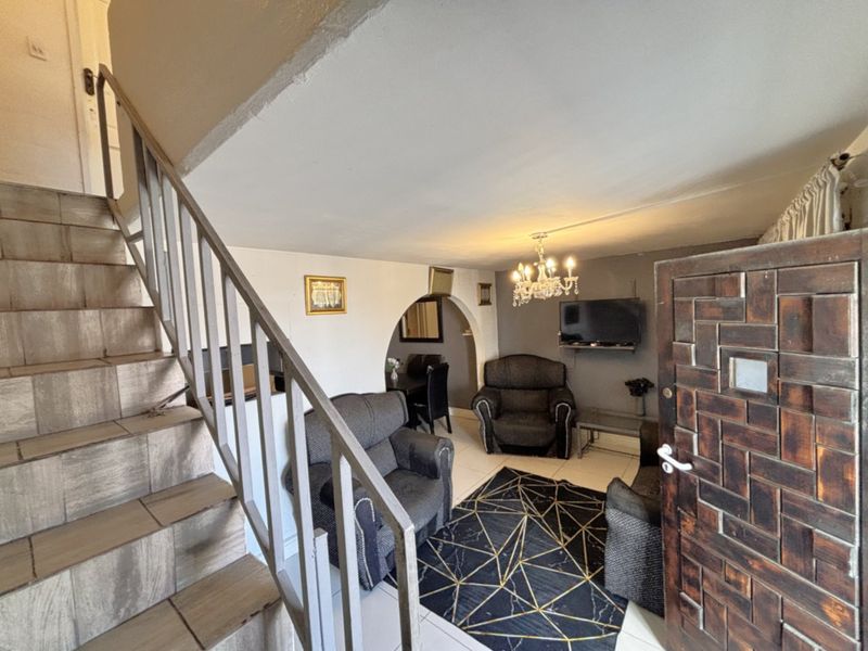 Living room area featuring a tiled staircase with metal balustrade, arched architectural detail, and tiled flooring, providing a functional open-plan layout.