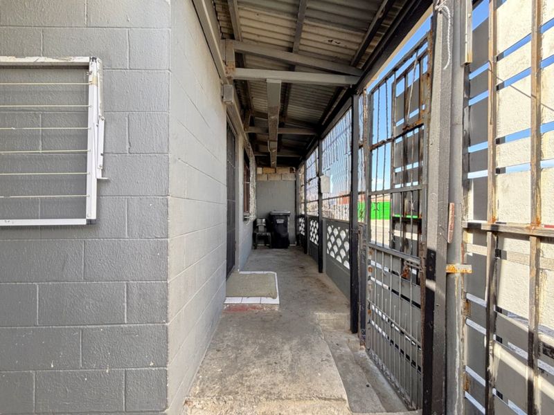 A covered outdoor walkway or patio area featuring concrete block walls, a corrugated metal roof, and a secure metal gate entrance.