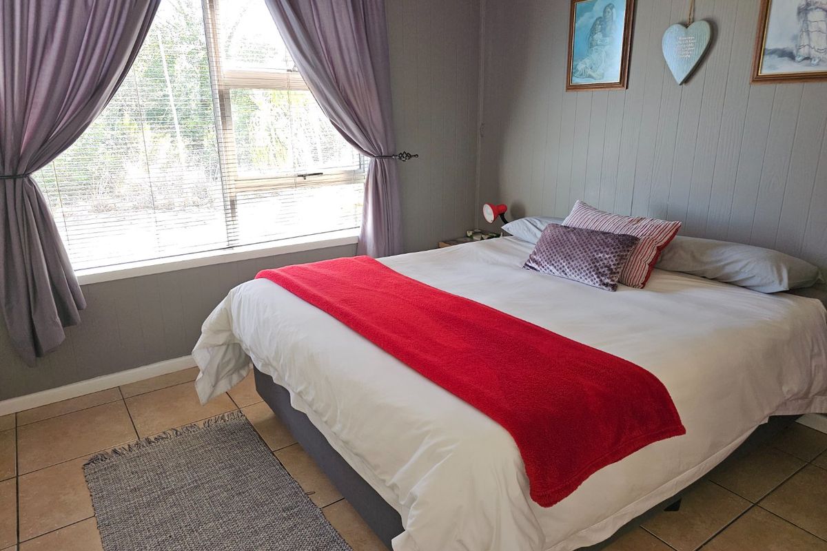 A bedroom featuring tiled flooring, vertical wall paneling, and a large window with horizontal blinds providing natural light.