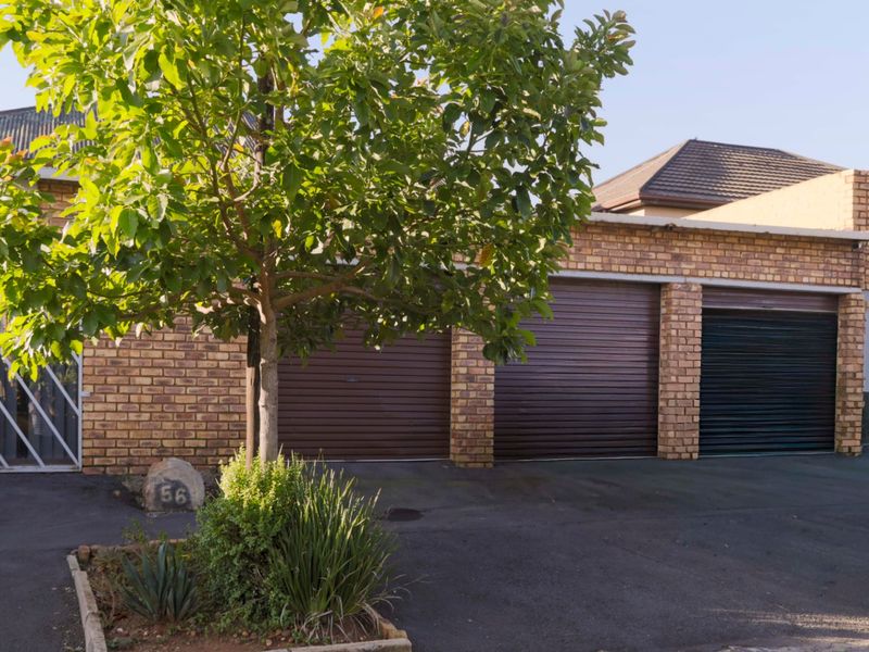 Front exterior view of the property featuring a triple garage with roller shutter doors, brick facade, and paved driveway.