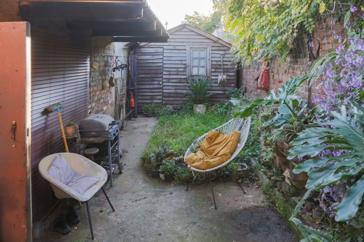 A rear garden area featuring a timber shed, brick boundary walls, and a concrete patio space with potential for landscaping and renovation.
