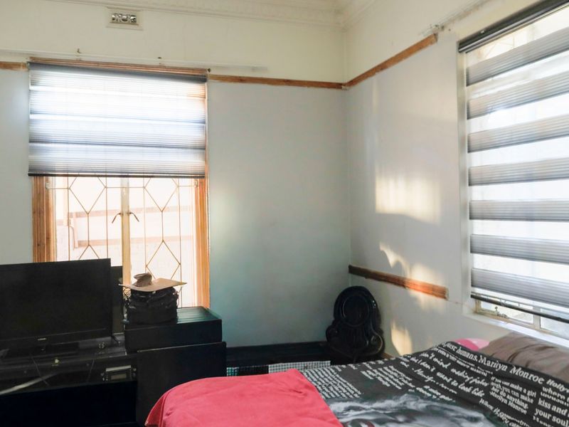 A bedroom featuring dual windows with zebra blinds, decorative cornicing, and picture rails, requiring cosmetic updates to improve the overall finish.