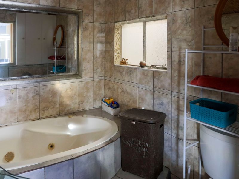 A bathroom featuring a built-in corner bathtub and tiled walls, offering potential for modernization and cosmetic updates to improve the overall aesthetic.