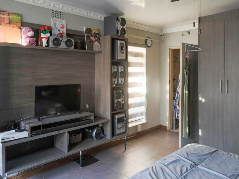 A bedroom featuring tiled flooring, built-in wardrobes, and decorative ceiling cornicing, offering a functional space with natural light from the window.