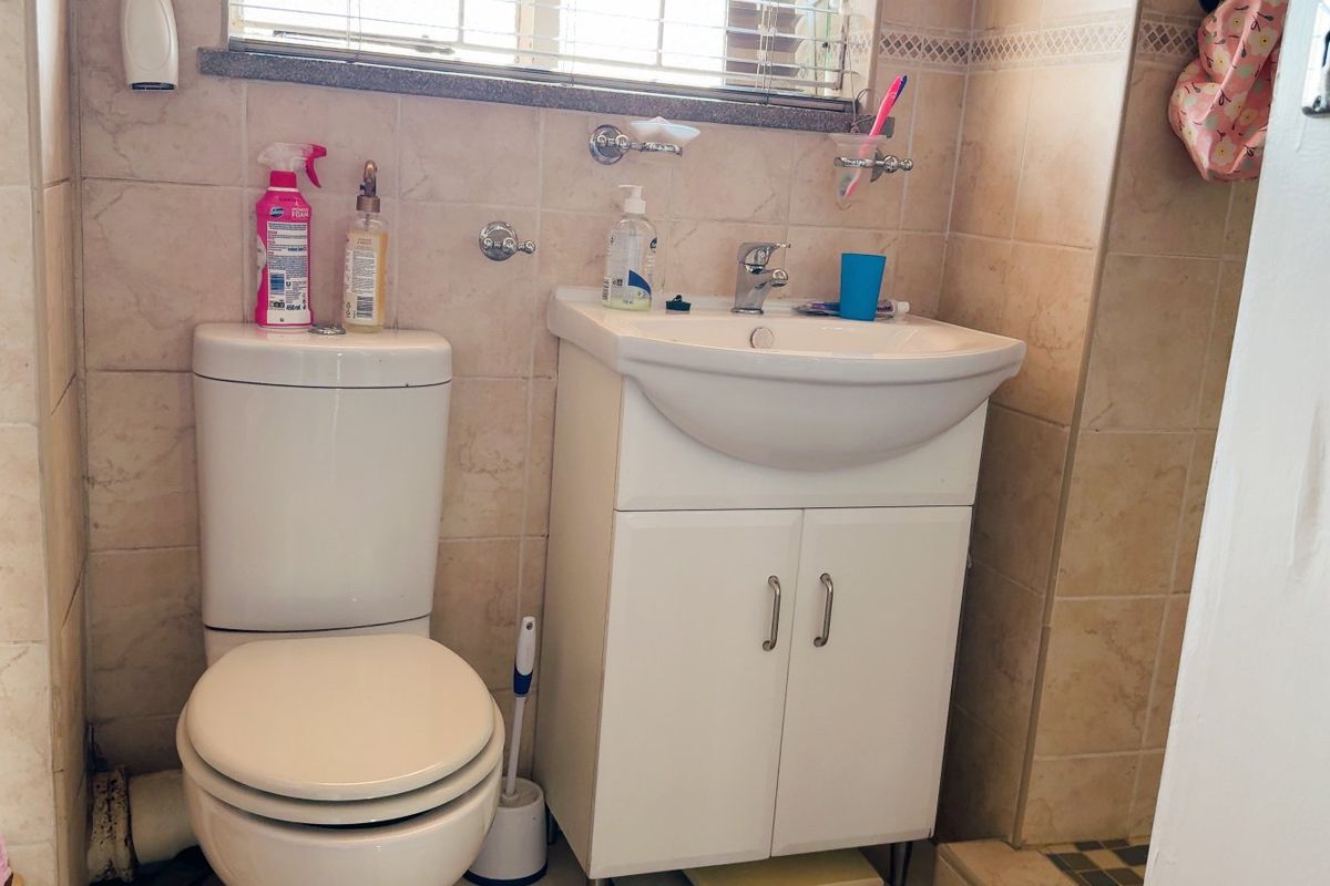 A functional bathroom featuring a white vanity cabinet with a ceramic basin, a standard toilet, and neutral wall tiling.
