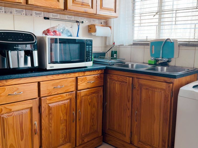 A functional kitchen featuring traditional wooden cabinetry, laminate countertops, a double stainless steel sink, and tiled backsplash with natural light from the window.