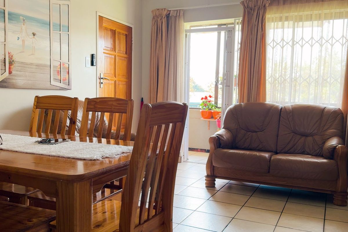 A living and dining area featuring tiled flooring, a timber door, and a sliding glass door leading to an outdoor space with security gate.