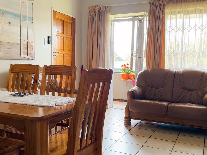 A living and dining area featuring tiled flooring, a timber door, and a sliding glass door leading to an outdoor space with security gate.