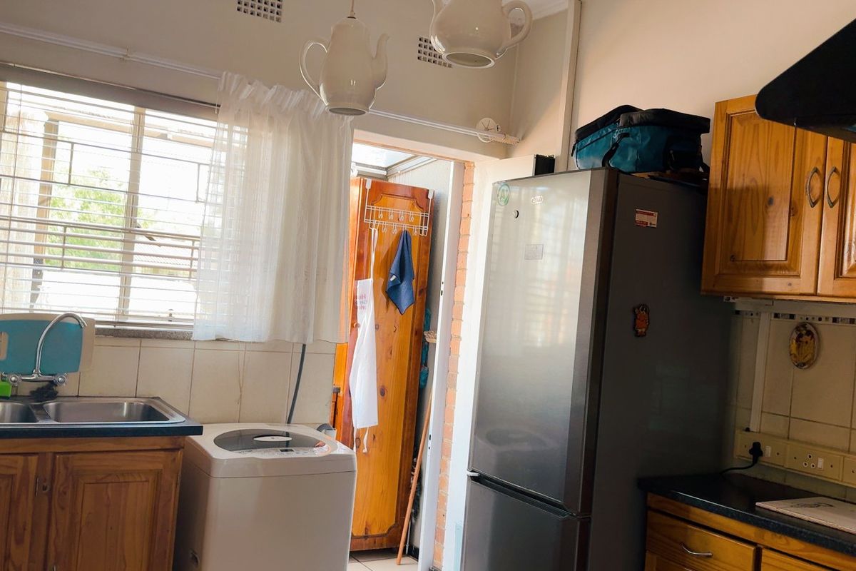A functional kitchen featuring wooden cabinetry, a double basin sink, tiled splashbacks, and an extractor fan, with natural light from the window.
