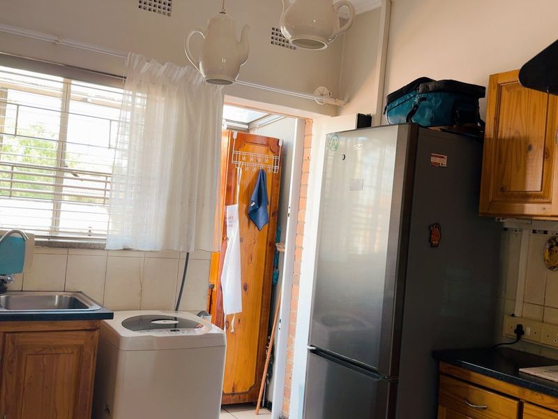 A functional kitchen featuring wooden cabinetry, a double basin sink, tiled splashbacks, and an extractor fan, with natural light from the window.
