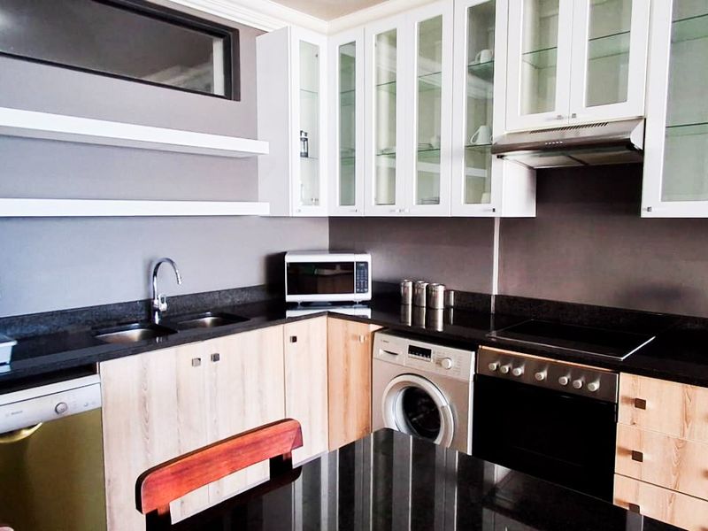 Modern kitchen featuring light wood cabinetry, contrasting black granite countertops, integrated appliances, and glass-front display cabinets.