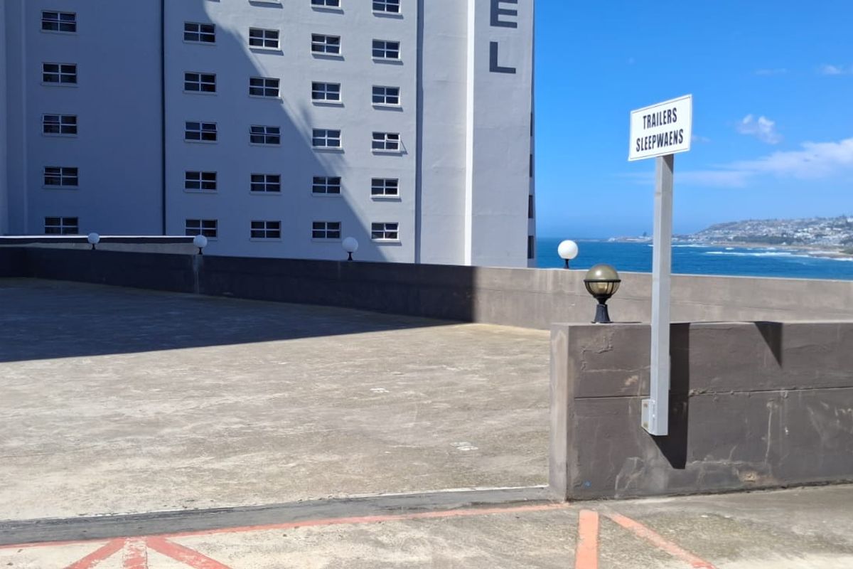 An open-air concrete terrace area featuring a low parapet wall, exterior lighting, and scenic coastal views adjacent to a high-rise building.