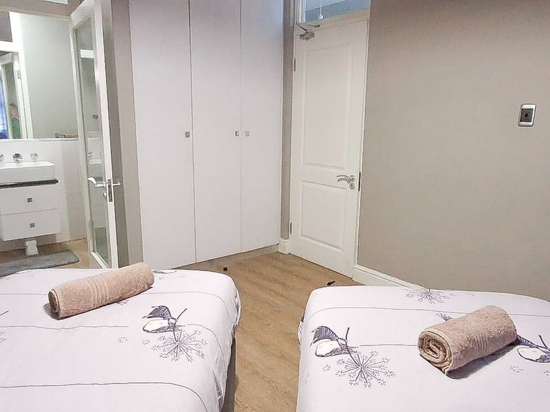 A bedroom featuring laminate flooring, built-in cupboards, and an adjoining en-suite bathroom with a modern vanity.