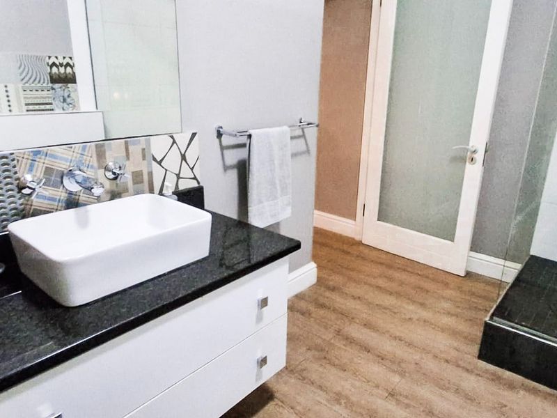 Modern bathroom featuring a white vessel sink on a granite vanity, walk-in shower with glass screen, and wood-look laminate flooring.