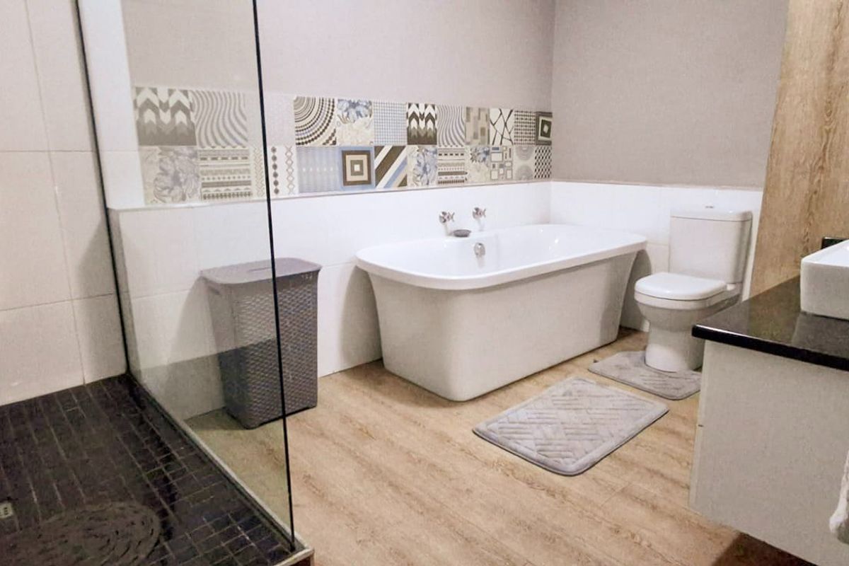 Modern bathroom featuring a freestanding bathtub, glass-enclosed shower, vanity with countertop basin, and decorative mosaic tile accents.