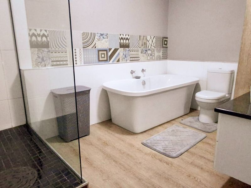 Modern bathroom featuring a freestanding bathtub, glass-enclosed shower, vanity with countertop basin, and decorative mosaic tile accents.