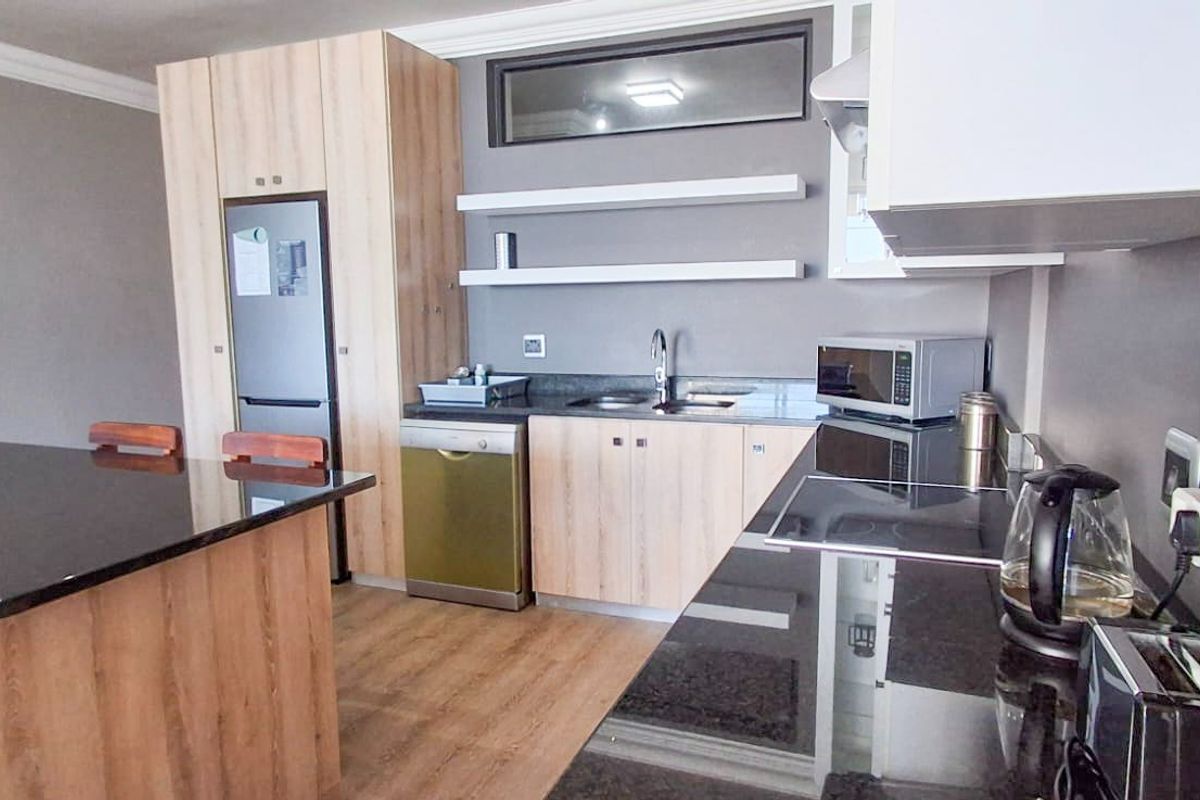 Modern kitchen featuring light wood cabinetry, sleek black granite countertops, an integrated island, and floating shelving, creating a functional and contemporary cooking space.