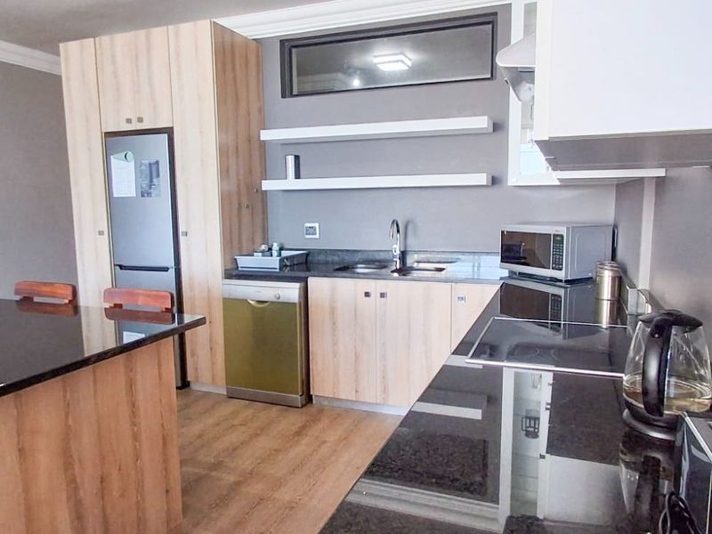 Modern kitchen featuring light wood cabinetry, sleek black granite countertops, an integrated island, and floating shelving, creating a functional and contemporary cooking space.