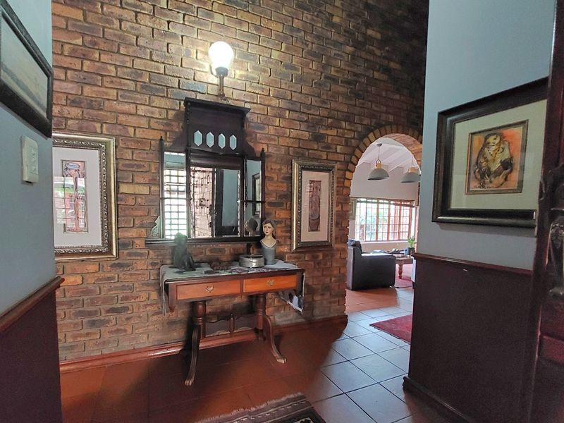 An inviting entrance hall featuring a rustic exposed brick wall, tiled flooring, and an arched transition leading into the main living area.