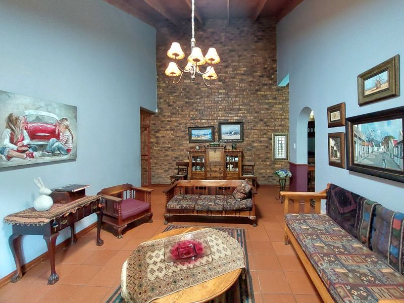 Spacious living room featuring a high exposed timber beam ceiling, a prominent face brick feature wall, and traditional terracotta floor tiles.