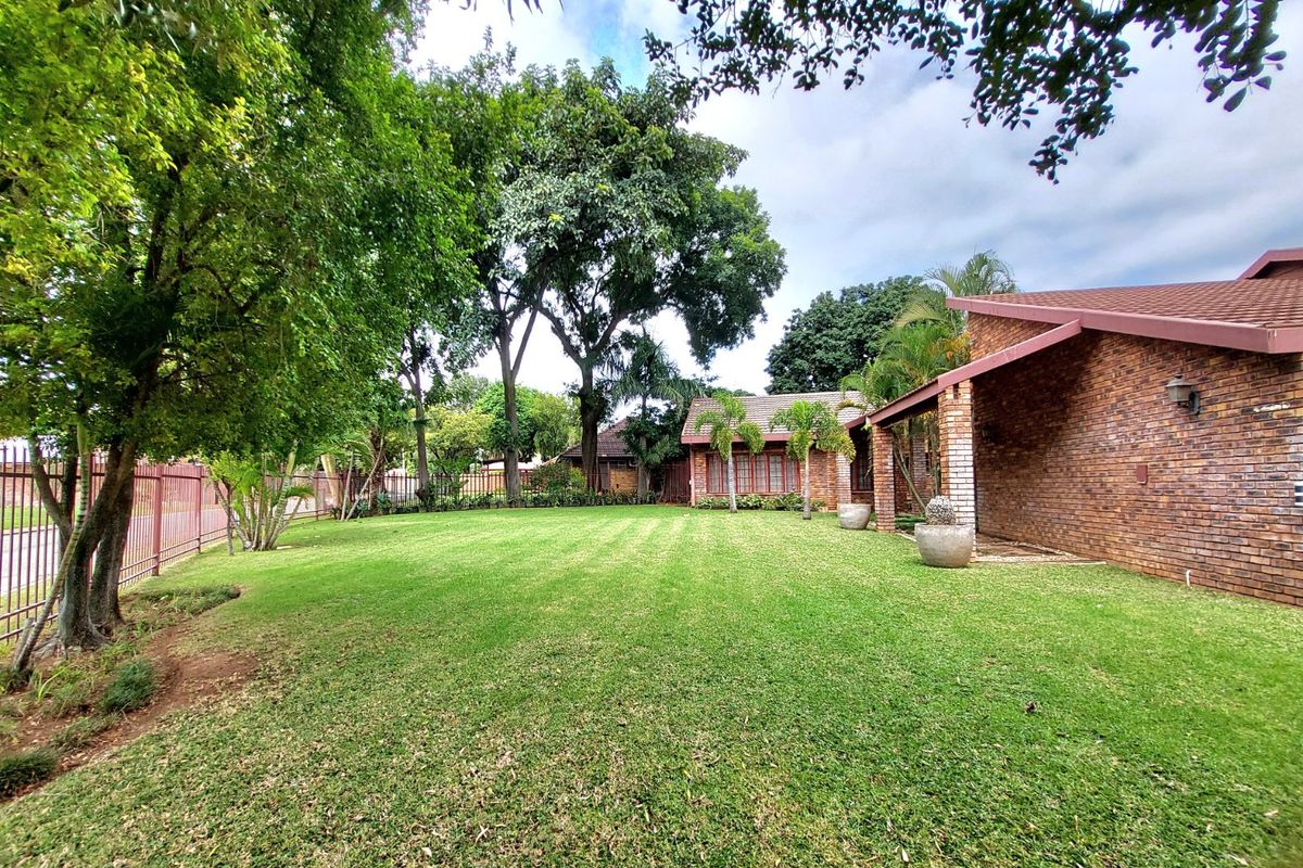 A well-maintained rear garden featuring a spacious lawn, mature trees, and a brick-built house with a covered patio area.