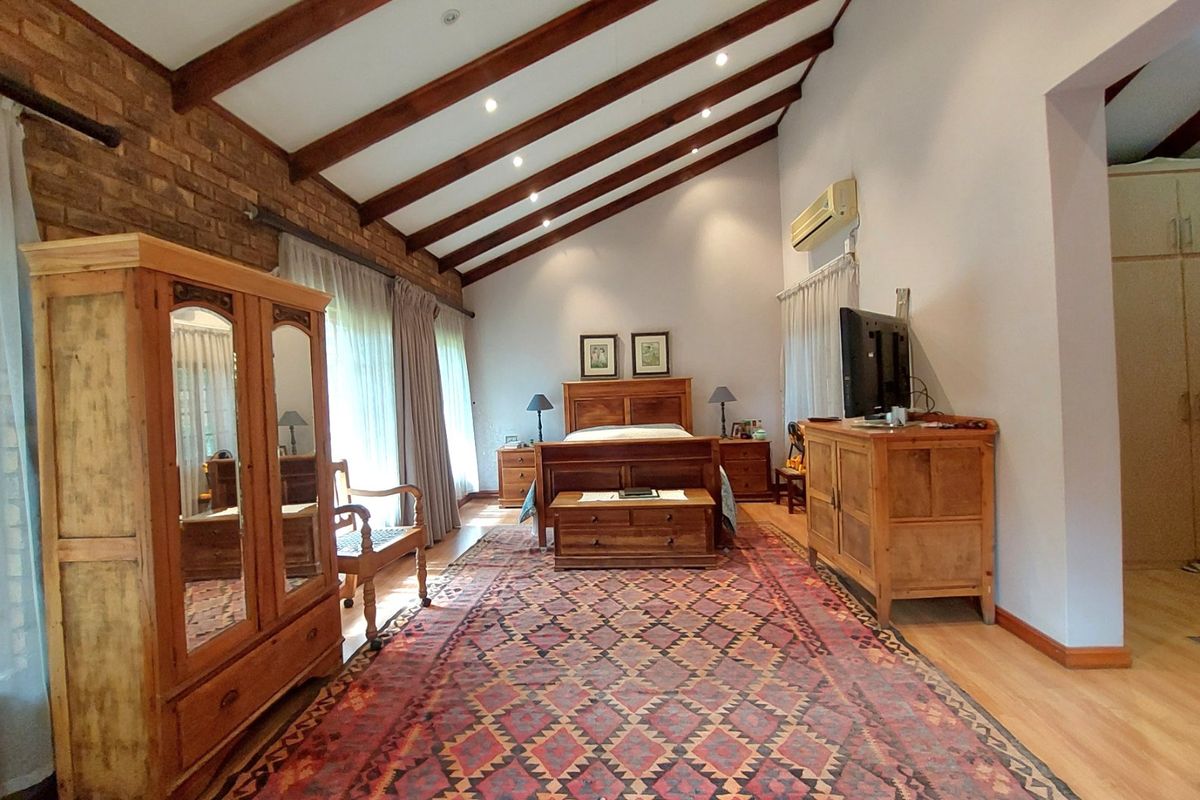Spacious bedroom featuring a vaulted ceiling with exposed timber beams, an exposed brick feature wall, and integrated air conditioning.