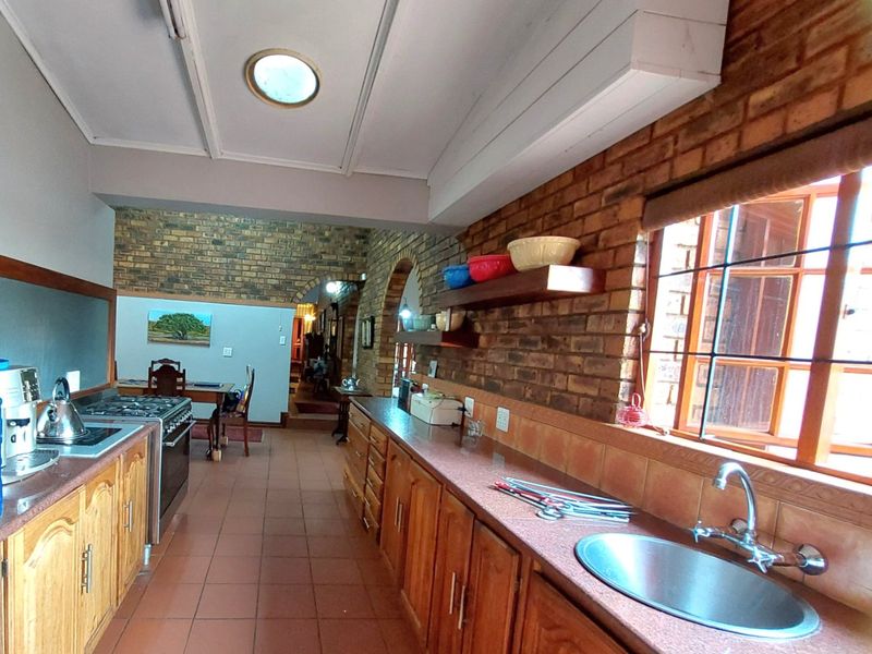 A rustic kitchen featuring exposed brick walls, wooden cabinetry, stone countertops, and a gas stove, with an open-plan flow leading to the dining area.