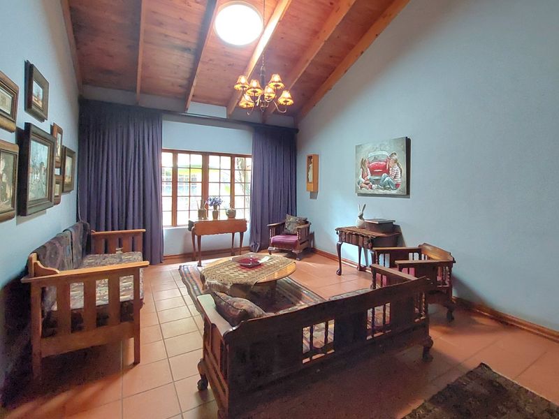 A spacious living room featuring exposed timber beam ceilings, terracotta floor tiles, and large windows, offering a warm and traditional aesthetic.