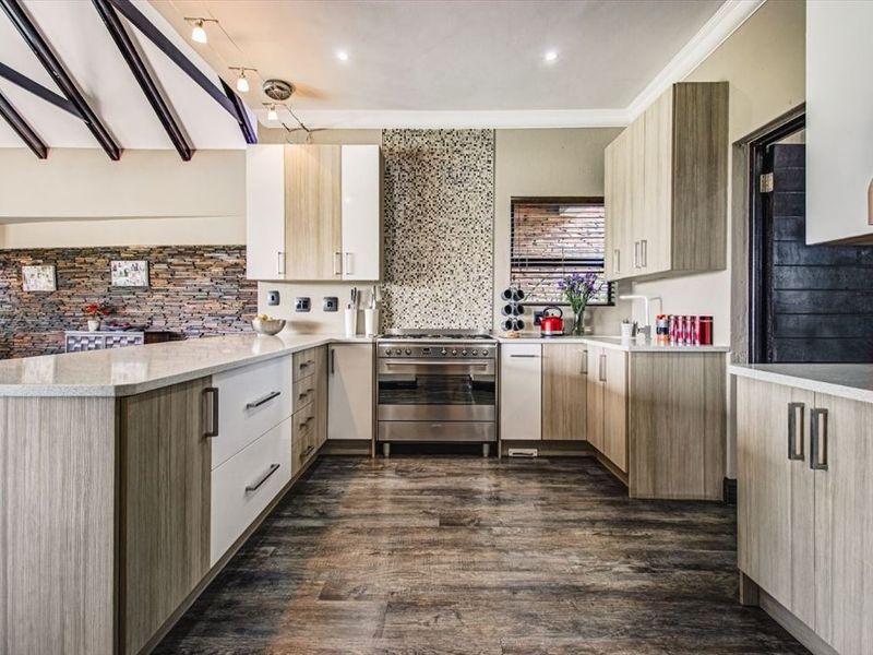 Modern kitchen featuring stone countertops, built-in cabinetry, a gas stove with mosaic splashback, and exposed timber ceiling beams.