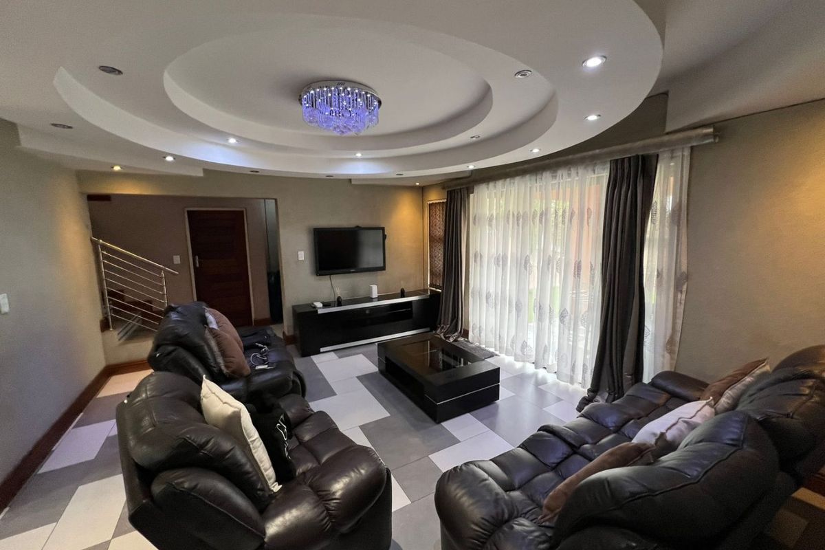 Spacious living room featuring a decorative recessed ceiling with downlights, tiled flooring, and large sliding glass doors providing access to the exterior.